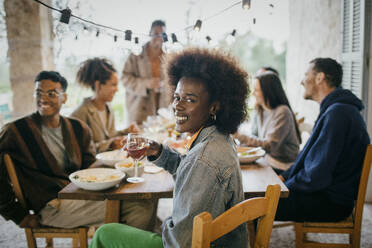 Porträt einer glücklichen Frau mit Afrofrisur, die ein Weinglas während einer Dinnerparty im Innenhof hält - MASF42936