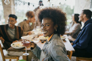 Lächelndes Porträt einer jungen Frau mit Afrofrisur, die ein Weinglas hält - MASF42937