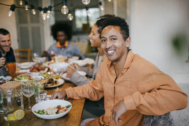 Porträt eines glücklichen Mannes, der während einer Dinnerparty im Innenhof am Esstisch sitzt - MASF42940