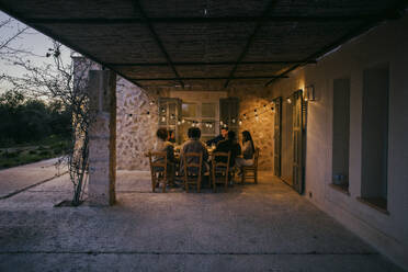Männliche und weibliche Freunde sitzen am Esstisch im Innenhof während einer Dinnerparty - MASF42945