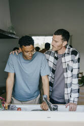 Mann steht mit Hand auf der Schulter eines Freundes in der Küche, gesehen durch ein Fenster - MASF42958