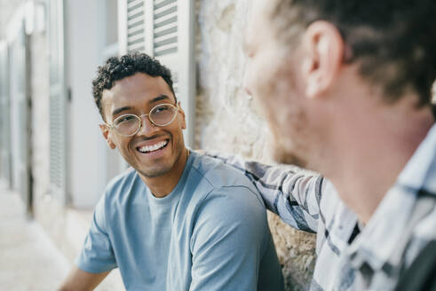 Smiling male friends talking while sitting at backyard - MASF42961