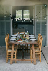 Glühbirnen hängen über einem Esstisch mit Stühlen auf einer Terrasse im Hinterhof - MASF42972