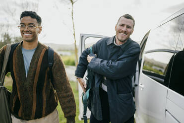 Lächelnde männliche Freunde mit Rucksäcken, die an einem Lieferwagen vorbeigehen - MASF42982