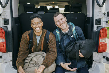 Porträt von glücklichen männlichen Freunden, die mit Gepäck im Kofferraum eines Lieferwagens sitzen - MASF42984