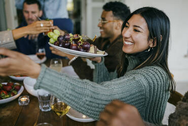 Lächelnde Frau mit Obstteller im Innenhof während einer Dinnerparty - MASF42992