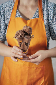 Woman wearing apron and holding chocolate ice cream in hand - TILF00067