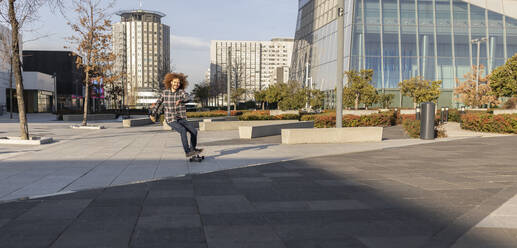 Glücklicher Mann auf dem Skateboard in der Stadt an einem sonnigen Tag - JCCMF11108