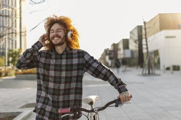 Glücklicher Mann hört Musik über drahtlose Kopfhörer und geht mit dem Fahrrad spazieren - JCCMF11111