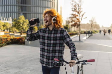 Glücklicher Mann hält Smartphone und hört Musik auf der Straße - JCCMF11116