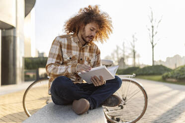 Ein Mann liest ein Buch und sitzt auf einem Sitz neben einem Fahrrad - JCCMF11120