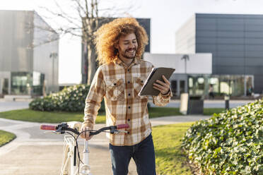 Happy man using tablet PC with bicycle on footpath - JCCMF11127