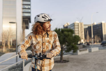 Man wearing helmet and standing with electric push scooter - JCCMF11132