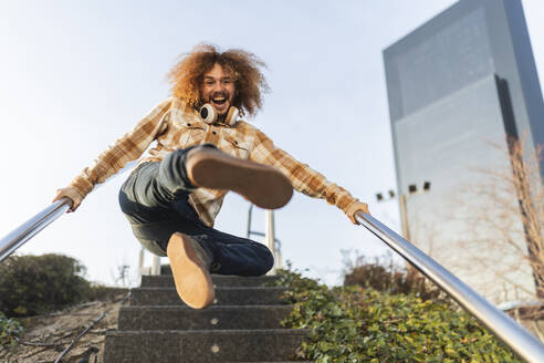 Happy man holding railing and jumping on staircase - JCCMF11142