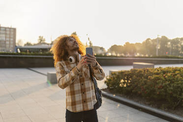 Happy man holding smart phone on footpath - JCCMF11145