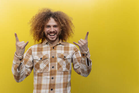 Happy man showing Shaka sign in front of yellow wall - JCCMF11154