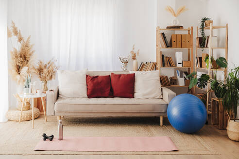 Gymnastikmatte auf dem Teppich neben dem Sofa und Fitnessball im Wohnzimmer - EBBF08525