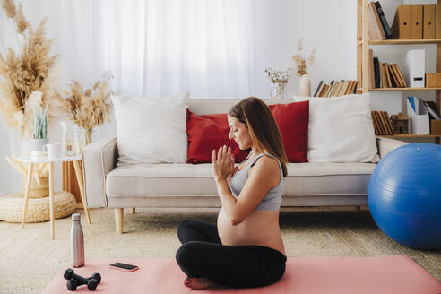 Schwangere Frau übt Yoga auf einer Übungsmatte zu Hause - EBBF08537