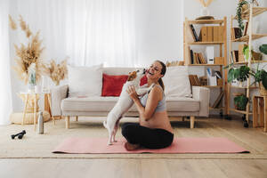 Glückliche schwangere Frau genießt es, dass ihr Hund sie zu Hause leckt - EBBF08554