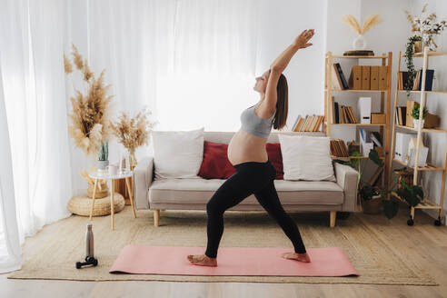 Schwangere Frau übt Yoga auf Matte im Wohnzimmer zu Hause - EBBF08574