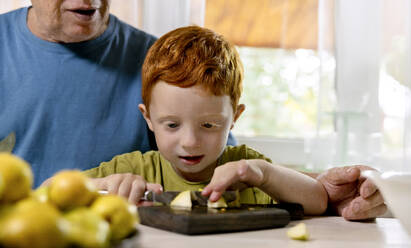 Junge lernt mit seinem Großvater zu Hause Früchte zu schneiden - MBLF00256