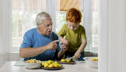 Großvater bringt seinem Enkel bei, wie man Obst zu Hause schneidet - MBLF00257