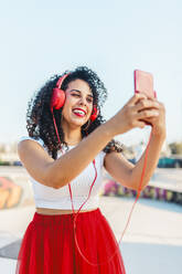 Glückliche Frau hört Musik und macht ein Selfie mit ihrem Smartphone im Skatepark - ASNF00010