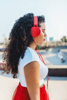 Frau mit geschlossenen Augen hört Musik über kabelgebundene Kopfhörer im Skatepark - ASNF00011