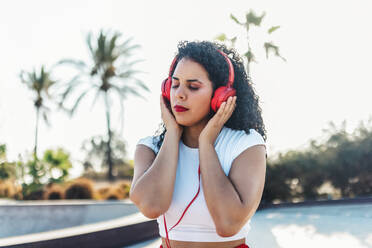 Frau mit geschlossenen Augen hört Musik über kabelgebundene Kopfhörer im Skatepark - ASNF00014
