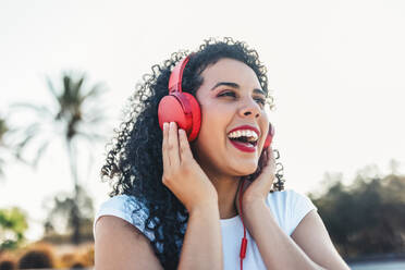 Cheerful woman listening to music through wired headphones at skateboard park - ASNF00015