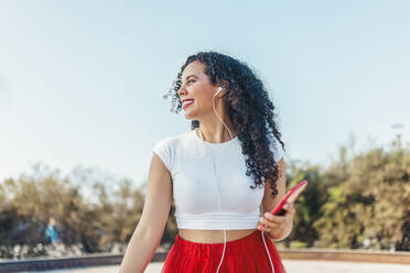 Smiling woman listening to music through in-ear headphones at skate park - ASNF00016