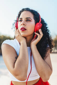 Nachdenkliche Frau hört Musik über kabelgebundene Kopfhörer im Skatepark - ASNF00017