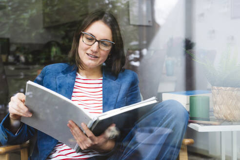 Geschäftsfrau beim Lesen von Berichten auf einem Stuhl im Heimbüro sitzend - IHF01885