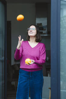 Lächelnde Frau, die mit Orangen jongliert, steht vor einer Haustür - IHF01891