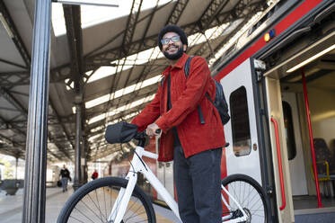 Lächelnder Mann mit Fahrrad in der Nähe des Zuges am Bahnhof - VRAF00377