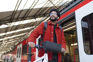 Nachdenklicher Mann hält Fahrradgriff in der Nähe des Zuges am Bahnhof - VRAF00378