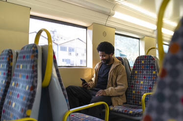 Lächelnder Mann mit Smartphone auf einem U-Bahn-Sitz sitzend - VRAF00384