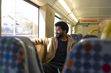Lächelnder Mann, der aus dem Fenster schaut, während er mit der U-Bahn fährt - VRAF00386