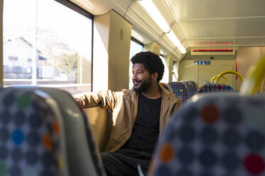 Smiling man looking out of window traveling in subway train - VRAF00386