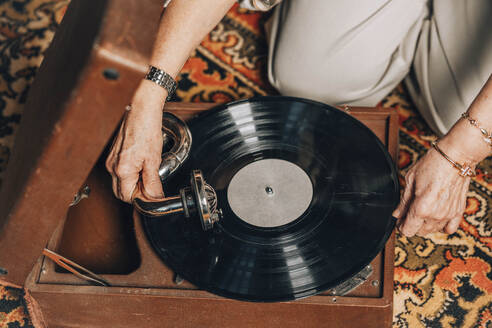 Senior woman using turntable on floor at home - ADF00280