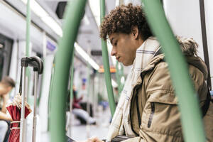 Young man with curly hair traveling in train - PBTF00485