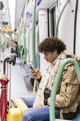 Mann mit Gepäck und Smartphone im Zug sitzend - PBTF00486