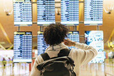 Mann mit lockigem Haar schaut auf die Abflugtafel am Flughafen - PBTF00487