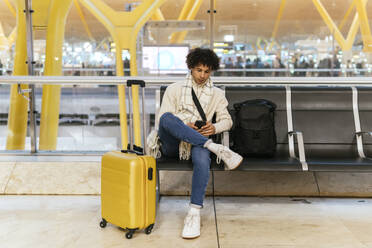 Man using smart phone sitting on chair at airport lounge - PBTF00490