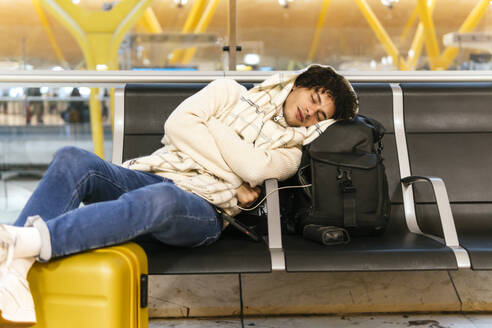 Young man taking nap leaning on backpack at airport lounge - PBTF00491