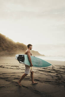 Junger Mann mit Surfbrett und Spaziergang am Strand - ACPF01560