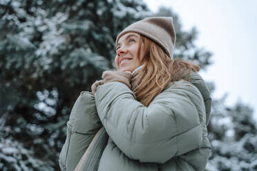 Lächelnde Frau mit warmer Kleidung und Tagträumen im Winter - NLAF00246