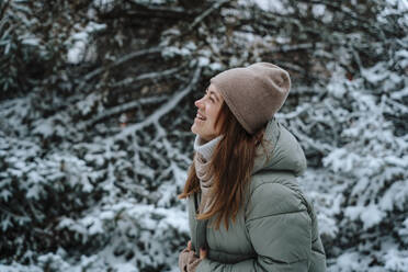 Cheerful woman laughing near trees in winter - NLAF00247