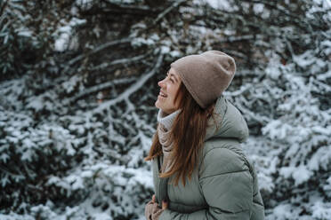 Fröhliche Frau lachend in der Nähe von Bäumen im Winter - NLAF00247