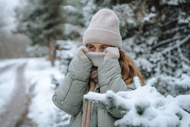 Playful woman covering face with sweater in winter - NLAF00250